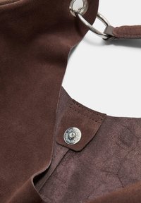 Brun ruskindsmateriale med en glat tekstur; har en sølv metal trykknap og en cirkulær metalring som accent.