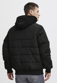 Sort puffer-jakke med hætte, quiltet design, ribbede manchetter og nederkant; båret med grå jeans og har en afslappet pasform.