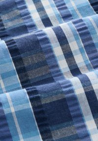 Tissu plié avec un motif à carreaux bleu, marine et blanc, avec des rayures de largeurs et textures variées.