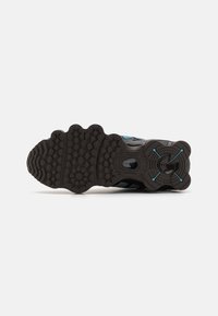 Black athletic shoe sole with textured rubber, shaped contours, blue accents, and hexagonal tread patterns for traction.