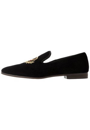 Chaussure slip-on en velours noir avec semelle plate et détail de couronne de laurier dorée brodée sur le dessus.
