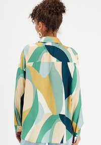Chemise à manches longues en tissu léger présentant des motifs abstraits audacieux et multicolores de vert, bleu, jaune et crème ; poignets à boutons.