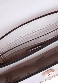 Interno di una borsa sintetica bianca con più scomparti, tra cui una tasca con zip e un rivestimento marchiato. Presenta una chiusura metallica rotonda.