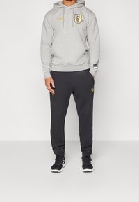 Harmaa huppari kultaisella logolla, yhdistetty tummiin housuihin, joissa on kultaisia yksityiskohtia. Asun täydentävät mustat urheilukengät. Yksinkertainen, rento design.