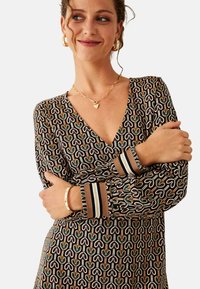 Vestido estampado con escote en forma de V, mangas largas con puños a rayas y un estampado de corazones geométricos en tonos tierra.