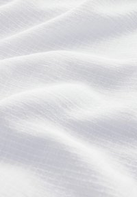 Tissu blanc au toucher léger et texturé, présentant un motif de carreaux subtil et des plis doux et fluides.