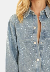 Veste en denim bleu clair avec des embellissements scintillants, y compris des strass et des accents d'étoiles, dotée d'une fermeture à boutons et d'un design western.