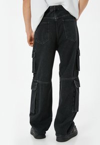Pantalones cargo negros de corte holgado, fabricados en denim, con múltiples bolsillos laterales y costuras decorativas en las costuras de las piernas y los bolsillos traseros.