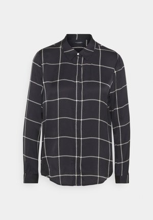 Camisa negra de manga larga con botones, patrón de cuadrícula blanca y cuello puntiagudo, presentada sobre un fondo liso de color gris claro.