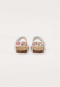 White sandals with floral pattern, adjustable straps, cork footbed, and textured rubber sole; features vibrant colors in the strap design.