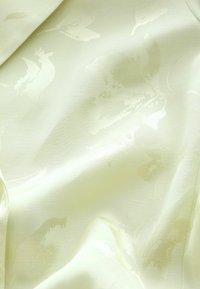 Tissu couleur crème avec un motif jacquard floral subtil et des plis doux, montrant une texture lisse et des reflets de lumière délicats.