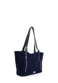 Navy suède totebag met twee metalen ritszakken, dubbele leren handvatten en een subtiele logo plaat. Gladde textuur en gestructureerde vorm.