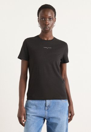 T-shirt en coton noir à col rond, manches courtes, avec le logo "TOMMY JEANS" en blanc centré sur la poitrine, associé à un jean bleu clair.
