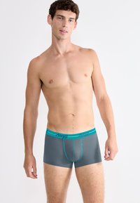 Grey men's boxer shorts with a contrasting turquoise waistband featuring the brand name "sloggi." Smooth, stretchy material, rectangular shape.