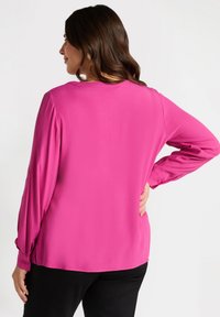Blusa rosa a maniche lunghe in tessuto morbido. Presenta un collo arrotondato, polsini con bottoni e una silhouette rilassata.