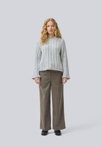 Pull en tricot gris clair avec un motif en torsade, manches larges, associé à un pantalon large vert olive et des chaussures noires.