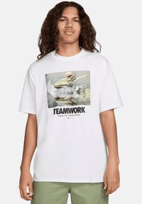 Camiseta de algodón blanca con un gráfico de una rana sobre una tortuga y el texto "EL TRABAJO EN EQUIPO HACE QUE EL SUEÑO FUNCIONE" en negro.