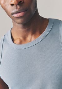 Canotta azzurro chiaro a coste con scollo tondo. Texture liscia con strisce strette, caratterizzata da una vestibilità confortevole e senza marchi visibili.