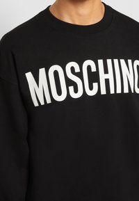 Černá Mikina vyrobená z bavlněné směsi s výrazným bílým textem "MOSCHINO" vpředu. Žebrovaný výstřih a manžety.