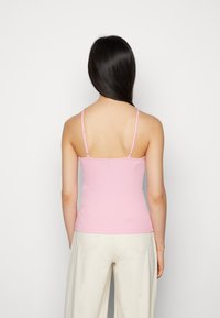 Top de alças ajustáveis finas, na cor rosa, feito de material de malha suave, apresentando um design simples e decote arredondado.