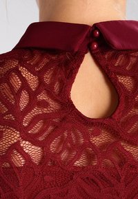 Burgunderfarbenes Spitzenkleid mit hohem Kragen, kunstvollen Blumenmustern, einem Schlüsselloch-Ausschnitt hinten und einem Knopfverschluss mit zwei dekorativen Knöpfen.