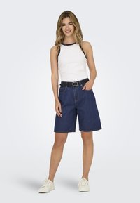 Shorts en denim avec une coupe décontractée, couleur bleu foncé, passants de ceinture, et une ceinture noire, assortis à un débardeur blanc avec des accents marine.