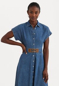 Denim skjortekjole med korte oppbrettede ermer, knappestolpe, belte i midjen med brun dobbeltspenne, og en full skjørt.