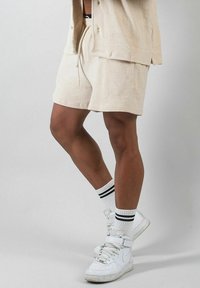 Beige frottéshorts med elastisk midja och snörning, kombinerade med vita högkostsnickers och vita strumpor med svarta ränder.