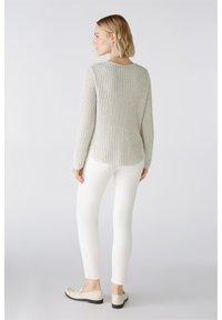 Helle graue, gerippte Strickpullover mit langen Ärmeln; kombiniert mit weißen, figurbetonten Hosen und hellen Schuhen, was ein lässiges Outfit unterstreicht.