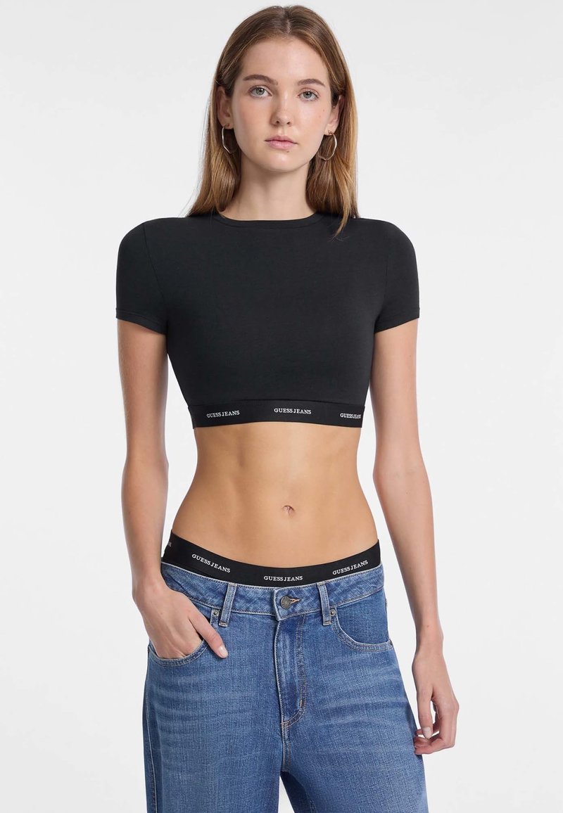 T-shirt nera corta con maniche corte, realizzata in materiale morbido. Presenta un orlo elastico brandizzato nero. Abbinata a jeans blu a vita alta.