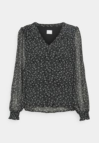 Svart blus med V-ringning, med genomskinliga långa ärmar och ett vitt prickmönster. Rynkade manschetter ger textur och detalj.