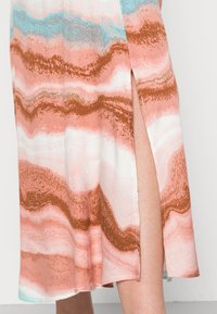Vestido estampado com listras onduladas em pêssego, branco e azul claro. Detalhe de fenda lateral que realça o movimento. Textura do tecido suave.
