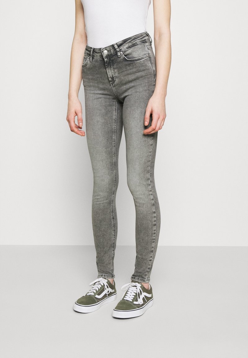 Grijze skinny jeans met een hoge taille, voorzien van de klassieke vijf-pocket stijl en een subtiele vervaging. Gedragen met groene en witte sneakers.