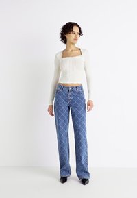 White ribbed long-sleeve top with square neckline paired with blue diamond-patterned jeans. Model wears black pointed-toe shoes.