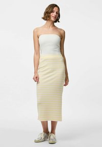 Bandeau ribbeltop, gecombineerd met een geel-wit gestreepte midirok. Het model draagt zilveren sneakers met veters. Eenvoudig en casual ontwerp.