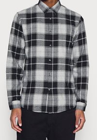 Černá a šedá kostkovaná košile s knoflíky vyrobená z tkané látky. Má límec, dlouhé rukávy a přední zapínání na knoflíky.