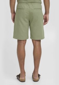 Grønne bomuldsshorts med snoreliv, der har to baglommer og en glat tekstur. Båret med brune sandaler.