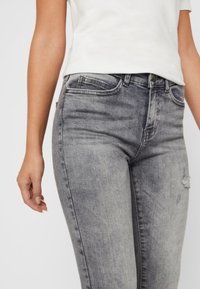 Jeans gris de tiro alto con un ligero desgastado, que presentan un clásico diseño de cinco bolsillos y un ligero detalle desgastado cerca de la rodilla.