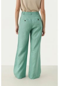 Pantalons larges de couleur vert clair en lin ; disposent de poches arrière à boutons et d'une taille haute. Texture douce et coupe décontractée.