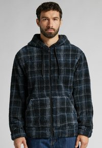 Hřejivá černá a modrá kostkovaná mikina na zip s kapucí, předními kapsami a detaily se stahovací šňůrkou; jemná textura a volný střih.