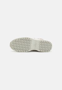 Semelle de chaussure en caoutchouc blanc avec un motif profond en forme de triangle, présentée sur un fond blanc uni.