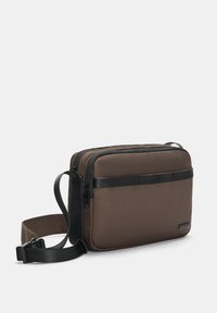 Braune Polyester-Crossbody-Tasche mit strukturiertem Finish, schwarzen Akzenten, zwei Reißverschlussfächern und einem verstellbaren Gurt.
