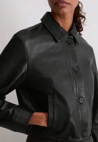 Czarna skórzana kurtka z klasycznym kołnierzem, zapięciem na guziki i bocznymi kieszeniami. Gładka struktura z dopasowaną sylwetką.