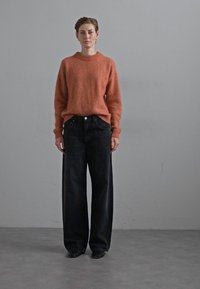 Rust-colored sweater in soft, fuzzy material paired with oversized black denim jeans. The outfit features a classic round neck and relaxed fit.