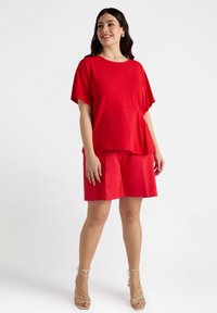 Red short-sleeve top with a layered hem paired with matching red shorts. The fabric appears soft and lightweight. Model wears strappy heels.