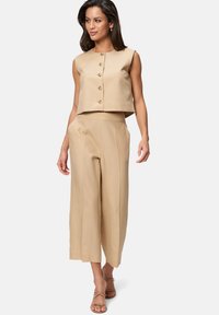 Ensemble beige en deux pièces comprenant un top sans manches court avec des détails de boutons et un pantalon large, le tout en tissu lisse.