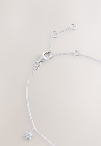 Silver chain necklace with lobster clasp and small star-shaped charm on light neutral background.