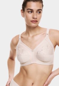 Sujeción beige con bordado floral, forma estructurada y tirantes ajustables. Cuenta con un pequeño adorno de flor decorativa en el centro.