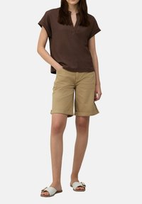 Bruine korte mouwen top met een kraag, gecombineerd met beige knielange shorts en witte slipper sandalen met een gouden accent.