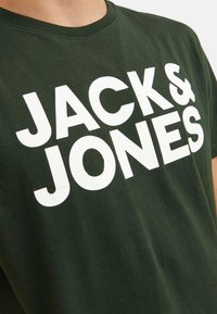 Dark green cotton t-shirt with a crew neckline, featuring large white text that reads "JACK & JONES" across the chest.
